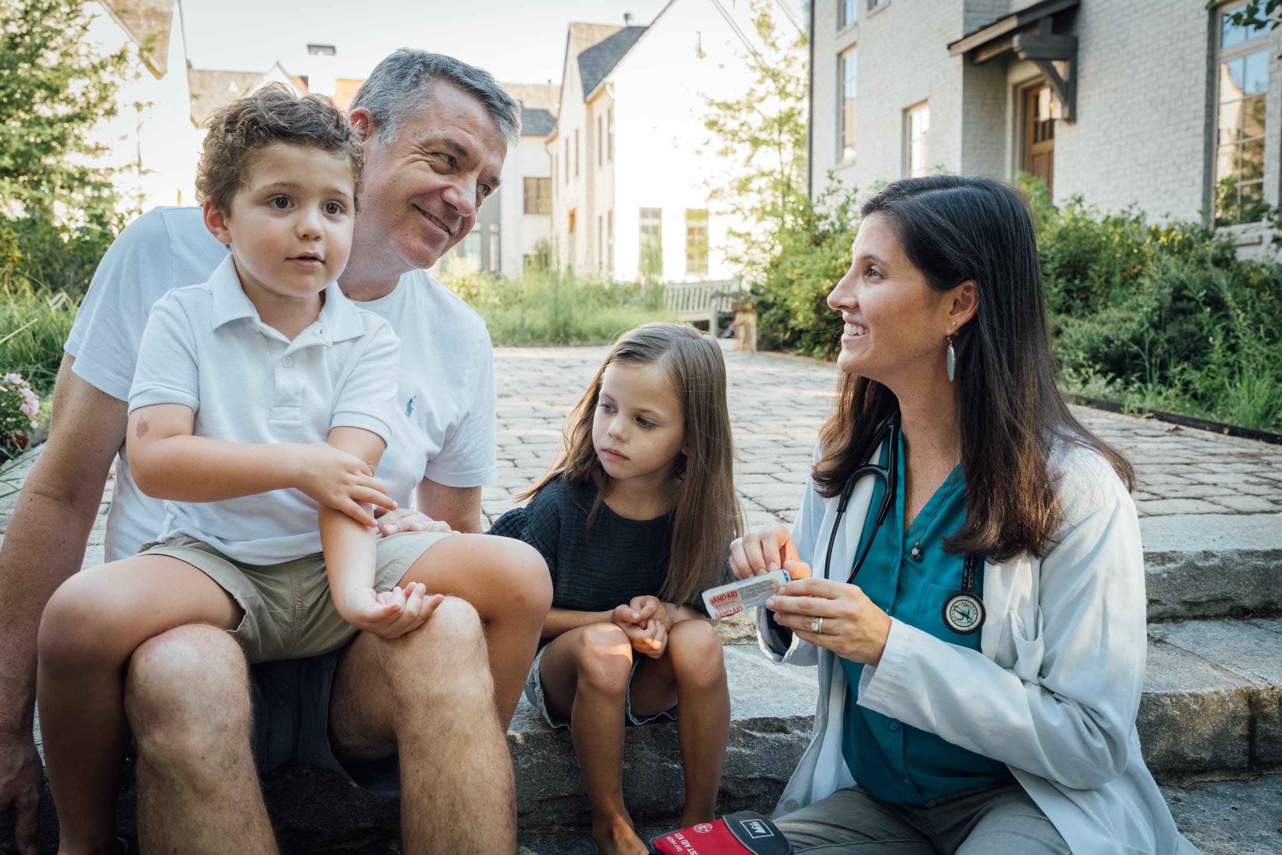 A pediatrician with a parent and child outside, treating a scraped arm